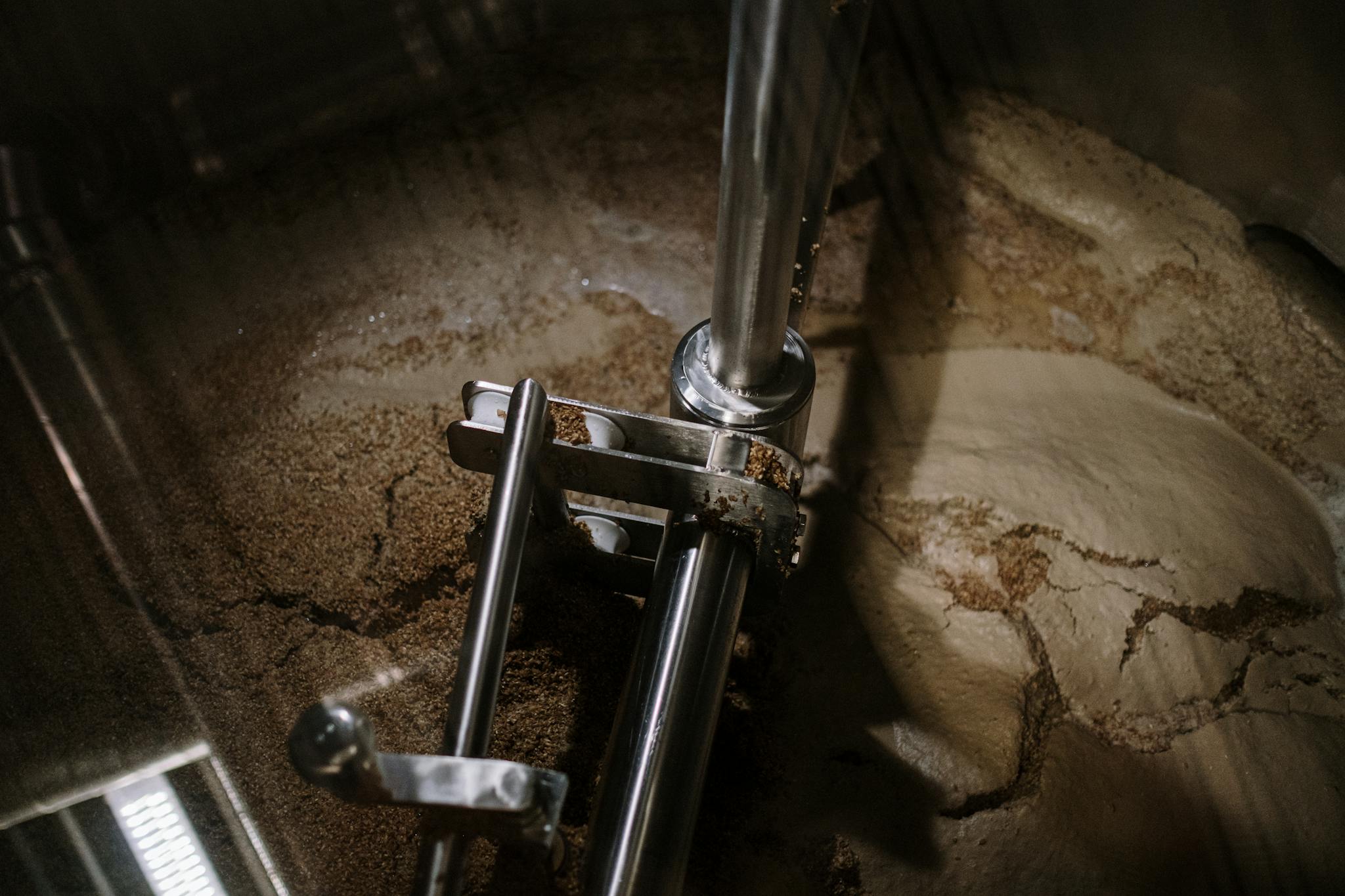 Close-up of a stainless steel industrial mixer stirring beer wort during fermentation in a brewery.